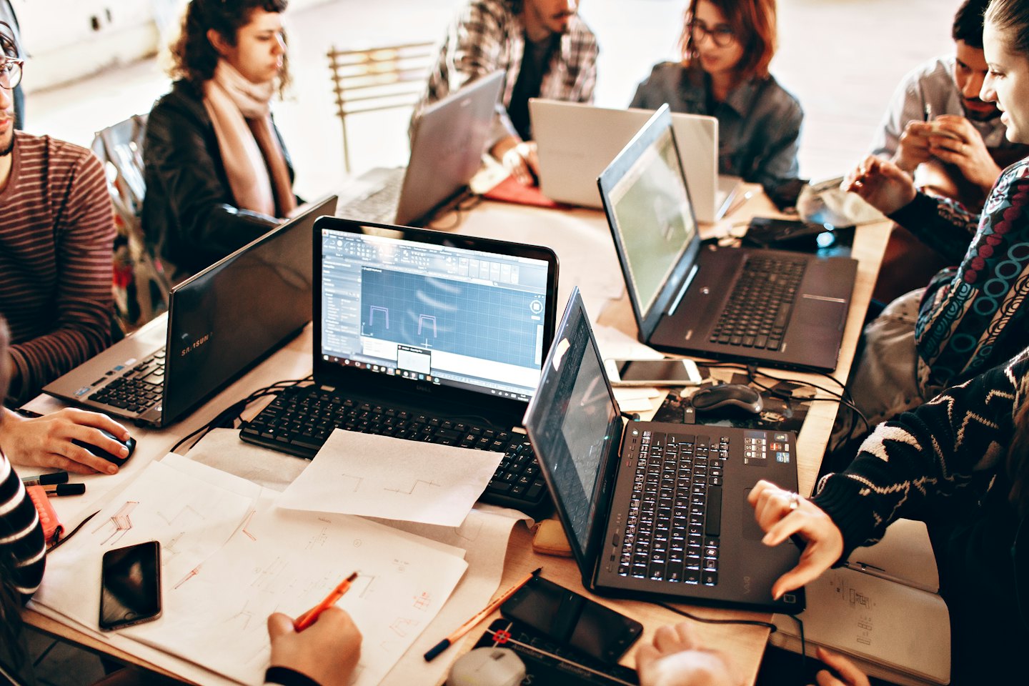 Giovani adulti diversi collaborano al computer portatile su un tavolo di legno.